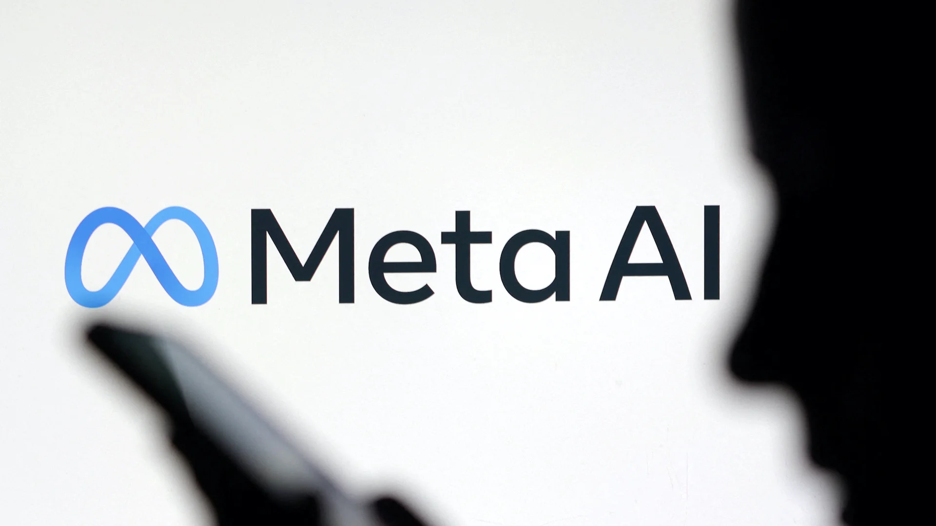 The Meta AI logo on a bright screen, with the silhouette of a person holding a phone in the foreground.
